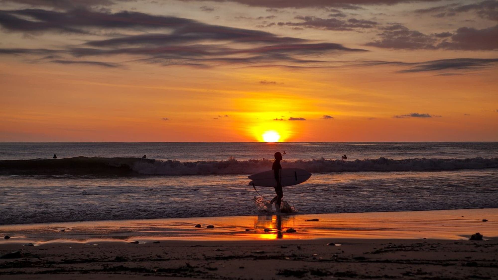 Silhouette of a surfer walking the beach at sunset